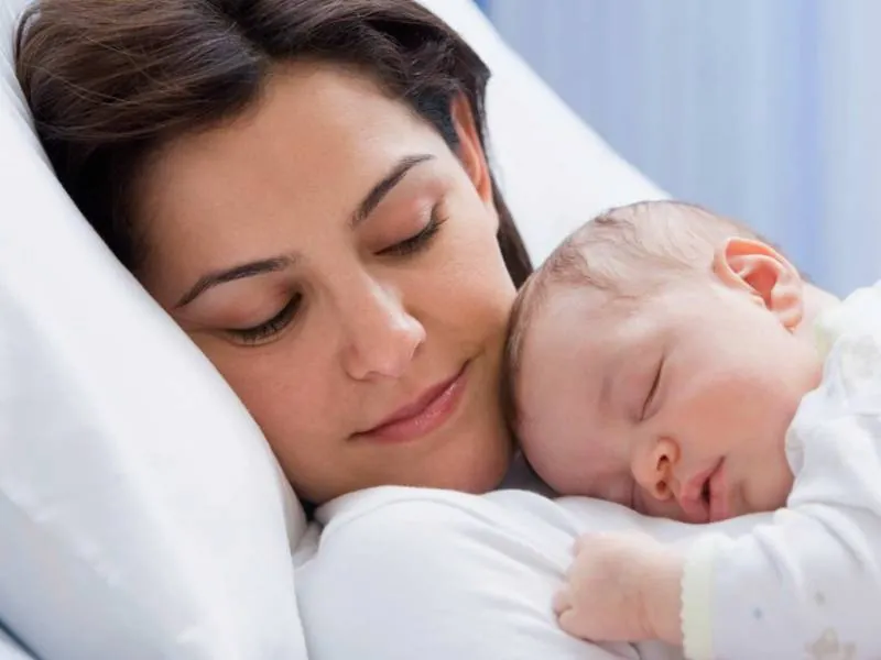 Stock photo of a mother resting on a white pillow with a sleeping newborn on her chest